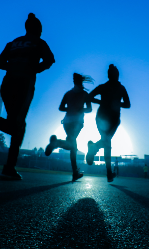 A low angle perspective image of three joggers running, their images are silhouetted by the sun in the background